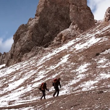 Two people hiking the Andes Mountains with hiking gear with a bottle of Terrazas de los Andes Reserva Malbec wine to enjoy a red wine at the top of the Aconcagua Summit