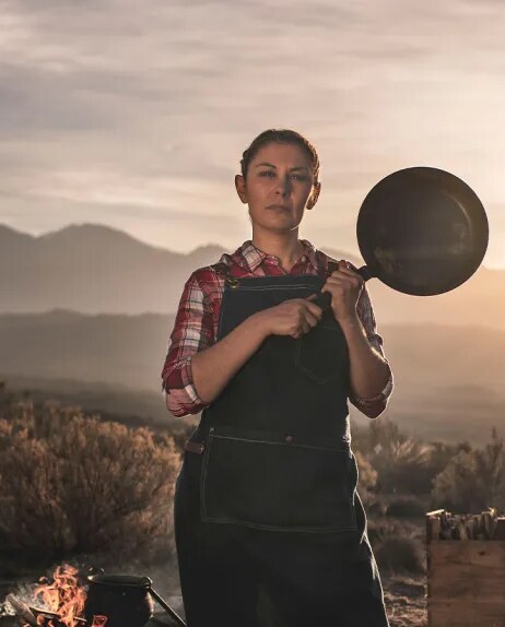 Una mujer en las montañas con una sartén de cocina en sus manos 