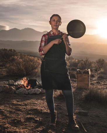 Noelia, Terrazas de los Andes Chef, is standing in front of the Mountains in Mendoza Argentina with a cooking pan