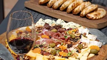  A table of cheese, ham, olives, next to a glass of red malbec wine from argentina